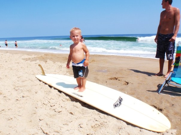 A young child standing on a surfboard at the beach in Kill Devil Hills, North Carolina
