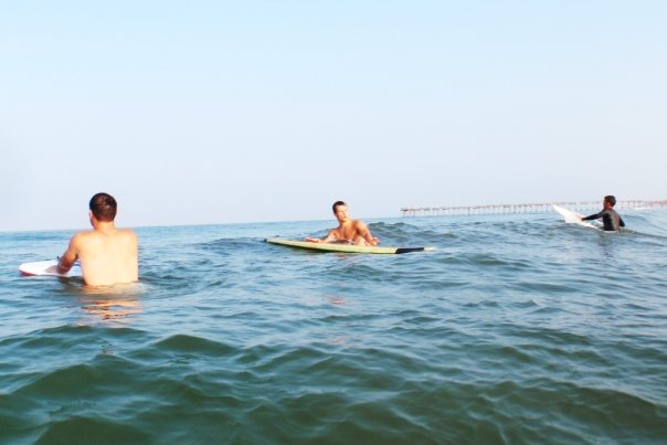 Three young men surfing near a pier in Nags Head, North Carolina