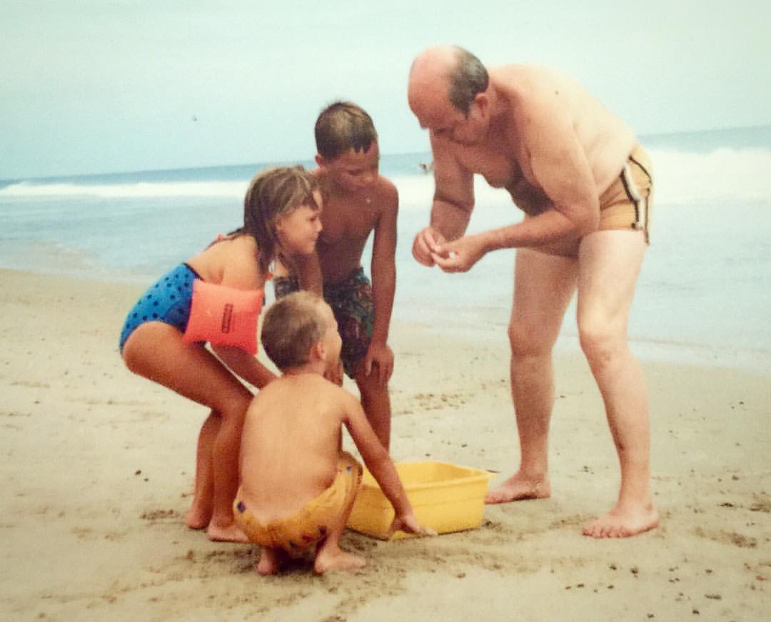 A man teaching his grandchildren about sand fleas at the beach in Southern Shores, North Carolina
